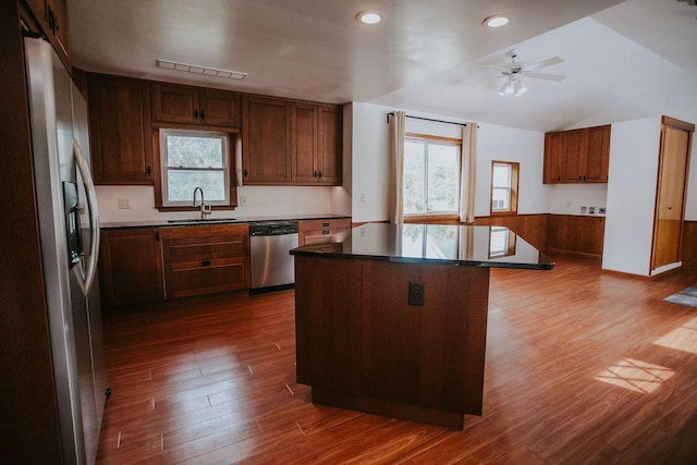 kitchen featuring a center island, dark wood-type flooring, wainscoting, appliances with stainless steel finishes, and a sink