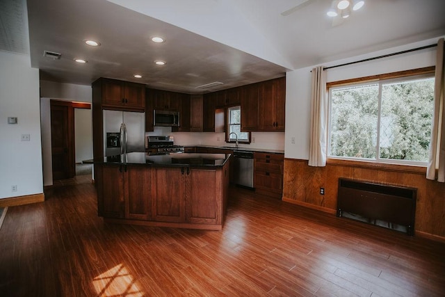 kitchen with a sink, appliances with stainless steel finishes, a center island, and dark wood-style flooring