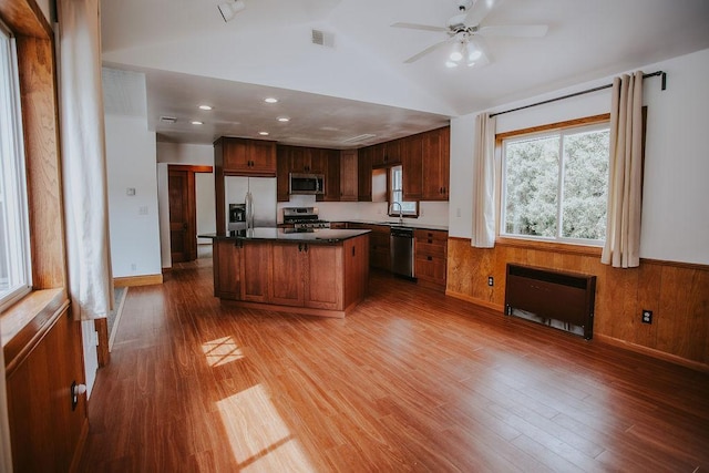 kitchen featuring stainless steel appliances, wood finished floors, a wainscoted wall, and vaulted ceiling