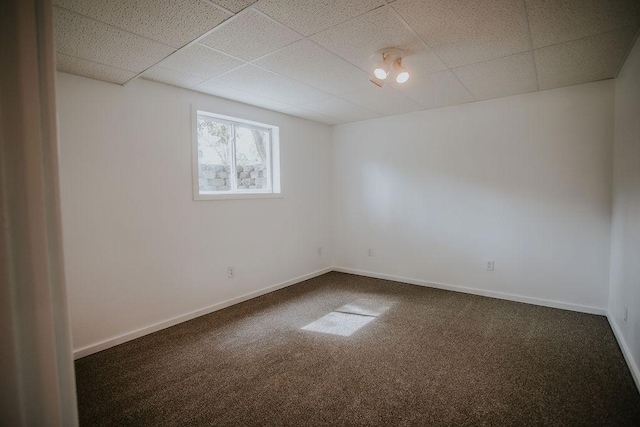 empty room featuring a drop ceiling, baseboards, and dark colored carpet