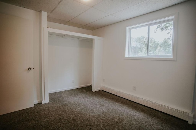 unfurnished bedroom with a baseboard heating unit, a paneled ceiling, baseboards, and dark carpet