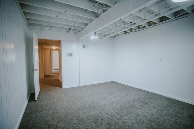 basement featuring wooden walls, visible vents, baseboards, and carpet floors