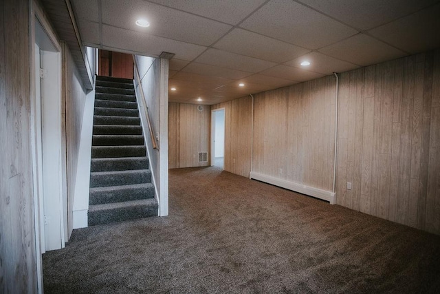 finished below grade area featuring stairs, carpet, wood walls, and baseboard heating