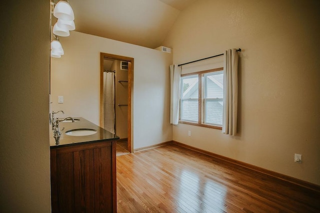 full bathroom featuring visible vents, baseboards, vaulted ceiling, wood finished floors, and a sink