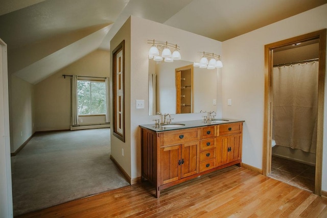 full bathroom featuring wood finished floors, a baseboard radiator, lofted ceiling, double vanity, and a sink