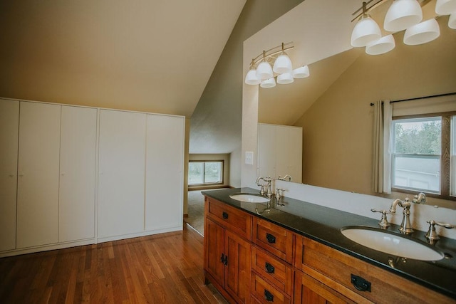 full bathroom featuring double vanity, wood finished floors, lofted ceiling, and a sink