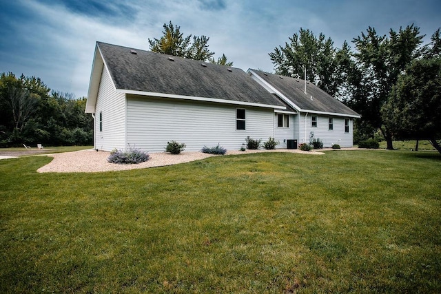 rear view of house featuring a lawn, central AC unit, and a shingled roof