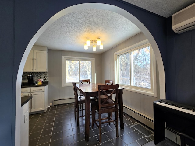 dining space with a textured ceiling, dark tile patterned flooring, a wall mounted AC, and a baseboard radiator