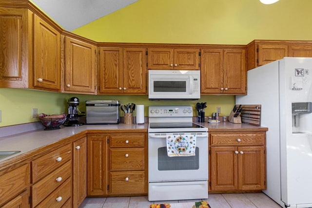 kitchen featuring white appliances, brown cabinets, vaulted ceiling, and light tile patterned floors