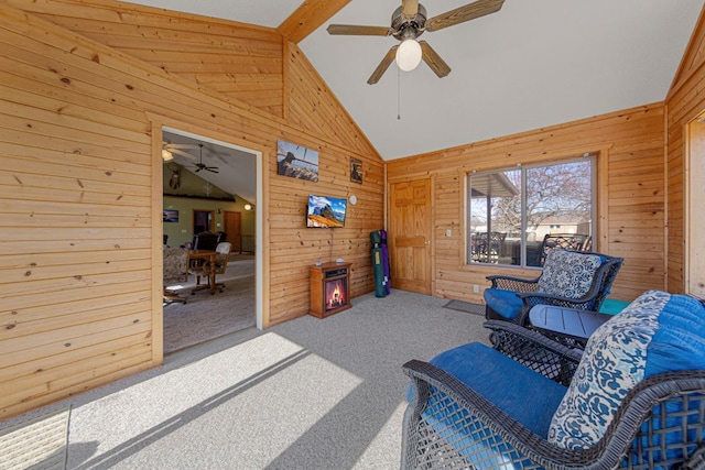 living area featuring carpet floors, high vaulted ceiling, wooden walls, and ceiling fan