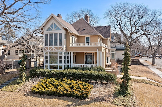 rear view of house with covered porch, stucco siding, a chimney, and a balcony