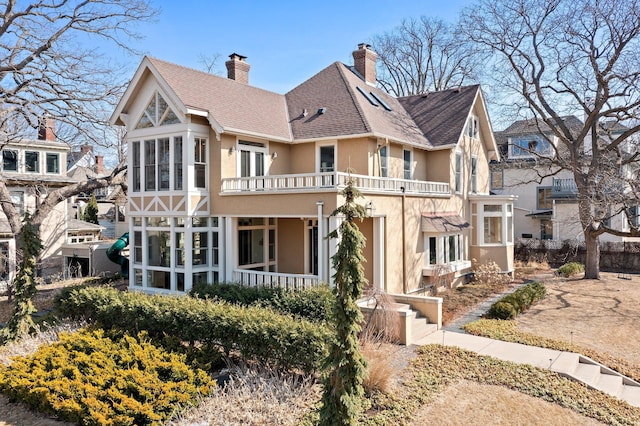 view of front of home with stucco siding, roof with shingles, a chimney, and a sunroom