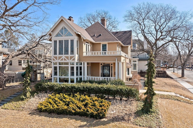 back of property with stucco siding, a balcony, covered porch, and a chimney