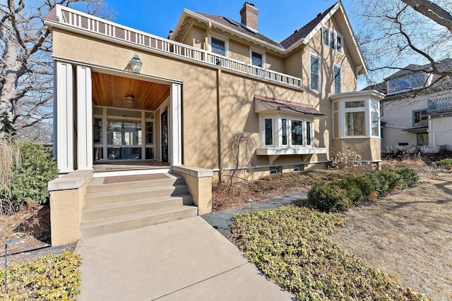 view of front of house featuring stucco siding, a porch, a chimney, and a balcony