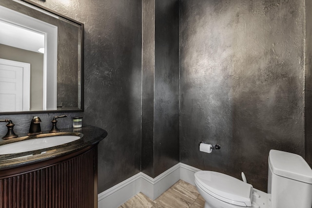 bathroom with vanity, toilet, and a textured wall