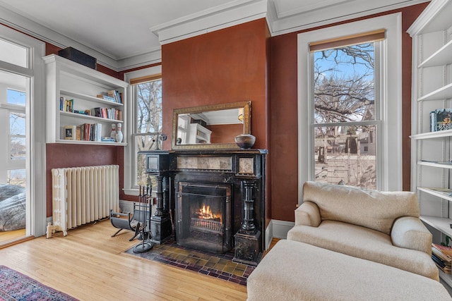 living area featuring a fireplace with flush hearth, ornamental molding, radiator, and wood finished floors