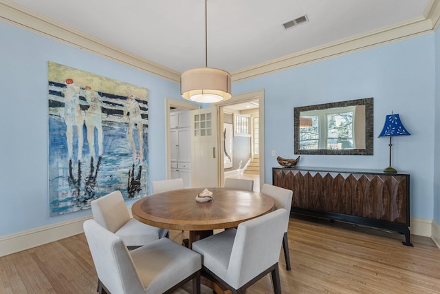 dining room with baseboards, visible vents, light wood-style flooring, ornamental molding, and stairs