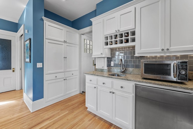 kitchen featuring a sink, light wood-style floors, white cabinetry, stainless steel microwave, and backsplash