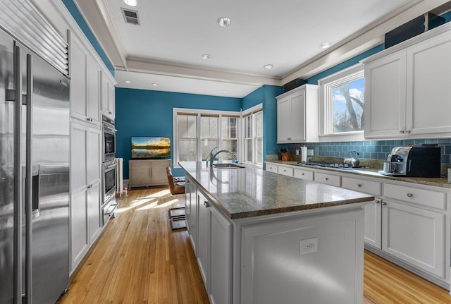 kitchen with backsplash, a center island with sink, light wood-type flooring, appliances with stainless steel finishes, and a sink