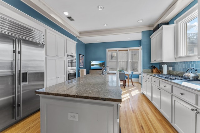 kitchen with visible vents, a sink, stainless steel appliances, white cabinetry, and a kitchen island with sink