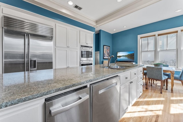 kitchen featuring visible vents, dark stone countertops, stainless steel appliances, white cabinetry, and a sink