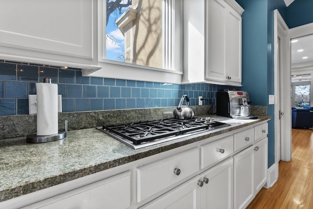 kitchen with backsplash, stainless steel gas stovetop, white cabinets, and light wood finished floors