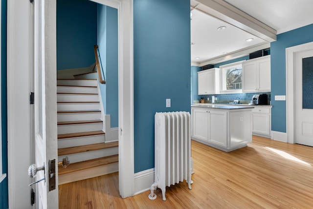 kitchen with decorative backsplash, white cabinets, radiator, and light wood-type flooring