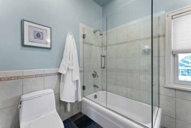 full bath featuring bath / shower combo with glass door, wainscoting, tile walls, toilet, and tile patterned floors