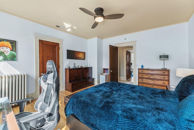 bedroom featuring light wood-type flooring, visible vents, radiator, crown molding, and ceiling fan