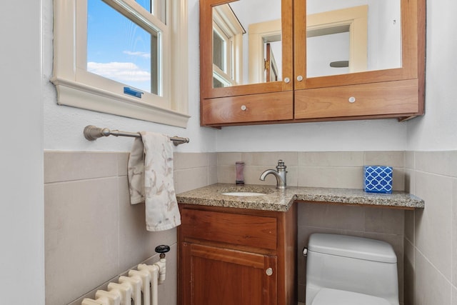 half bathroom with radiator, a wainscoted wall, toilet, vanity, and tile walls