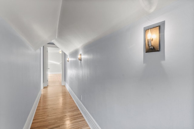 hall featuring light wood-type flooring, lofted ceiling, and baseboards