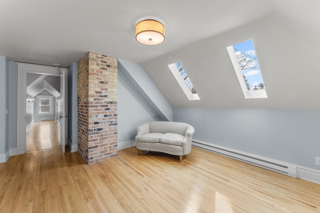 living area with vaulted ceiling with skylight, wood finished floors, baseboards, and baseboard heating