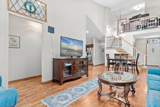 living area with baseboards, stairway, wood finished floors, a towering ceiling, and an inviting chandelier