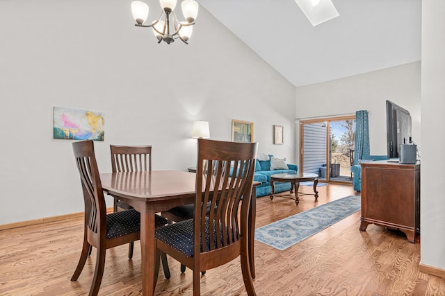 dining room with an inviting chandelier, a skylight, wood finished floors, and high vaulted ceiling