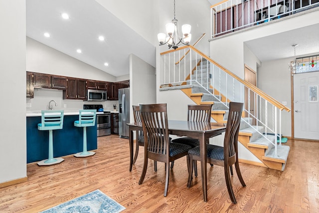 dining room featuring an inviting chandelier, stairway, light wood-style floors, and high vaulted ceiling