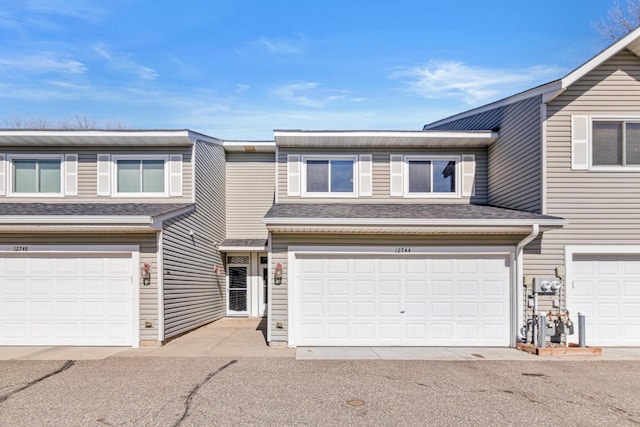 multi unit property featuring a garage and roof with shingles