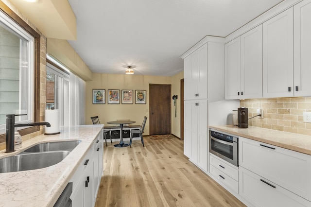 kitchen with light wood finished floors, decorative backsplash, white cabinets, a sink, and oven