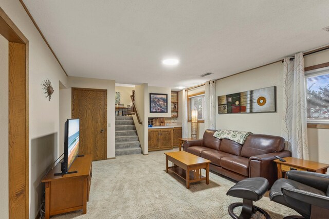 living room featuring stairway, visible vents, and light colored carpet