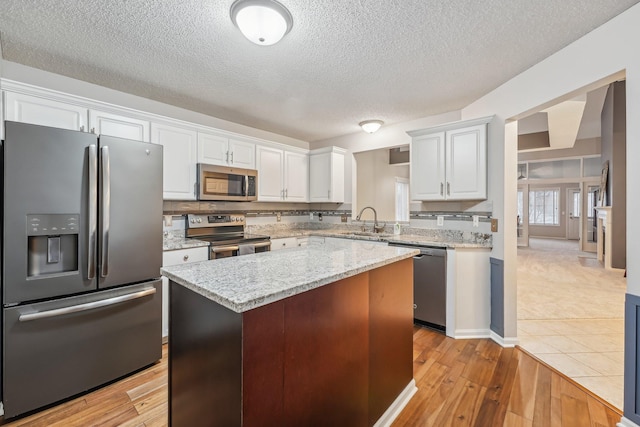 kitchen featuring a center island, stainless steel appliances, white cabinets, a sink, and light wood-type flooring