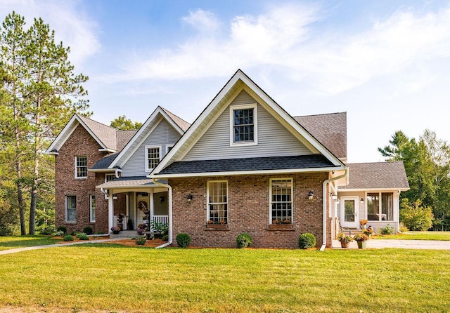 view of front of house featuring roof with shingles, a front yard, a porch, and brick siding