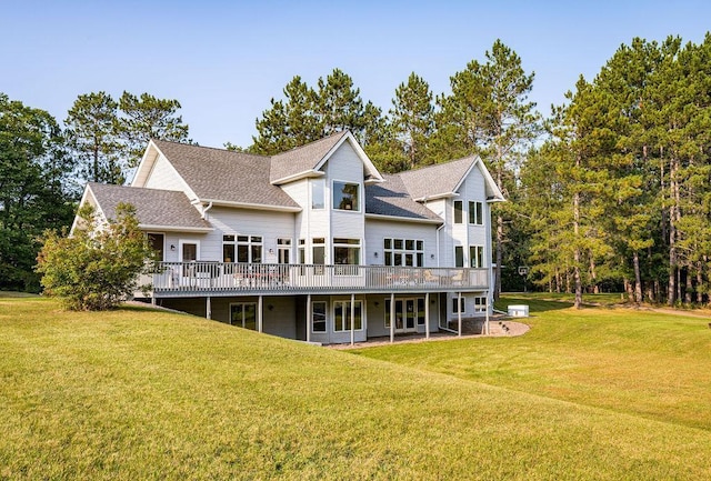 rear view of house featuring roof with shingles, a lawn, and a wooden deck