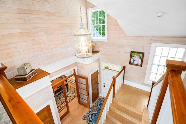 stairs featuring lofted ceiling, wooden walls, and wood finished floors