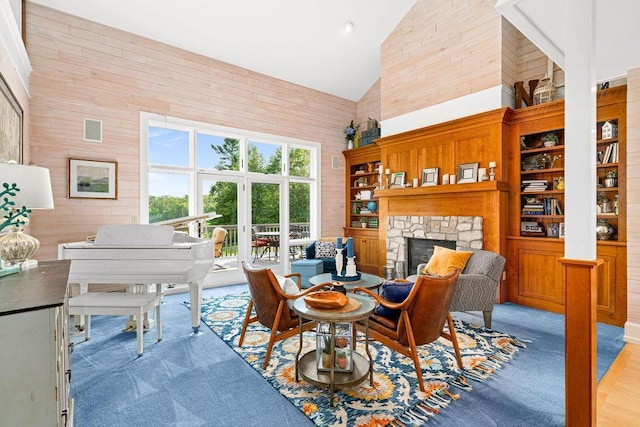 living area featuring high vaulted ceiling, a stone fireplace, wood walls, visible vents, and carpet