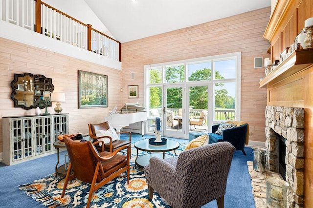 carpeted living area with wood walls, high vaulted ceiling, and a stone fireplace