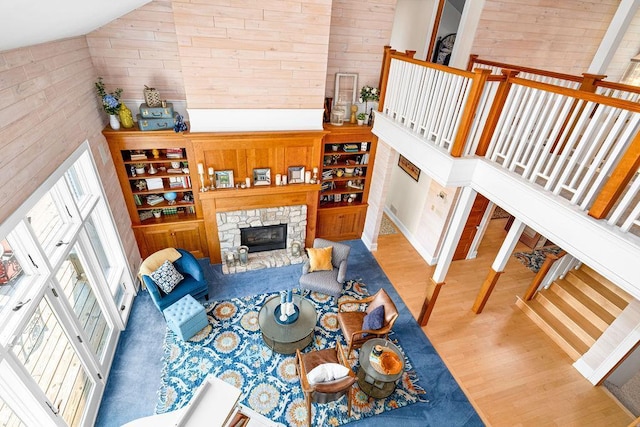 living room featuring high vaulted ceiling, a stone fireplace, wood finished floors, and wooden walls