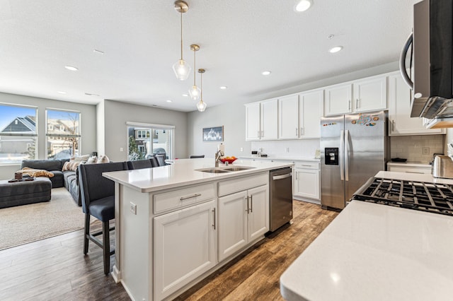 kitchen featuring a sink, open floor plan, appliances with stainless steel finishes, decorative backsplash, and an island with sink