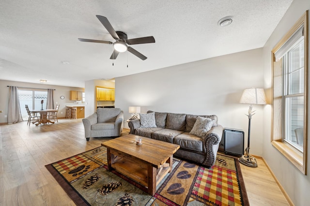 living area featuring light wood-type flooring, ceiling fan, baseboards, and a textured ceiling