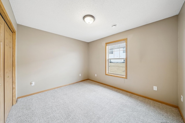 unfurnished bedroom featuring a closet, light colored carpet, a textured ceiling, and baseboards