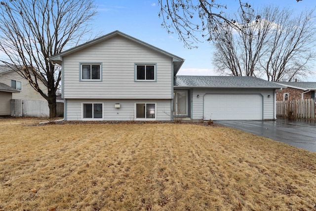 split level home with a garage, driveway, a front lawn, and fence