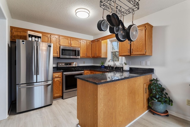 kitchen featuring a peninsula, brown cabinetry, stainless steel appliances, and light wood-style floors